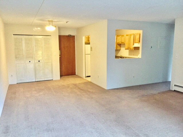 an empty living room with a mirror and a refrigerator